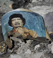 A picture of former Libyan dictator Muammar Qadhafi is seen in the ashes during fighting in Libya in 2011. Two years after the uprising that led to the overthrow of the Libyan government, the country still has not begun eliminating thousands of pounds of mustard blister agent loaded in artillery rounds during the now-deceased leader’s regime (AP Photo/Bela Szandelszky).